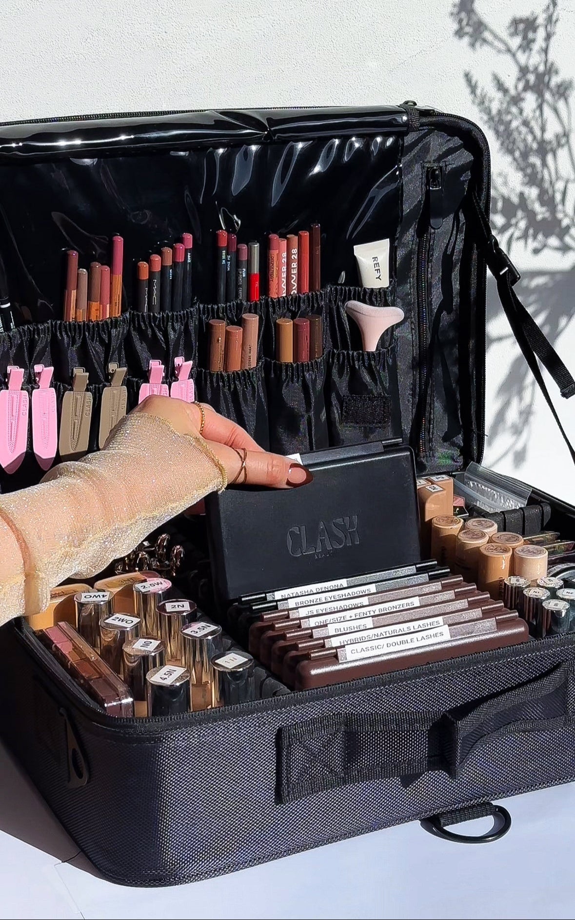 Black makeup case with various cosmetic items including brushes and palettes, held open by a hand.
